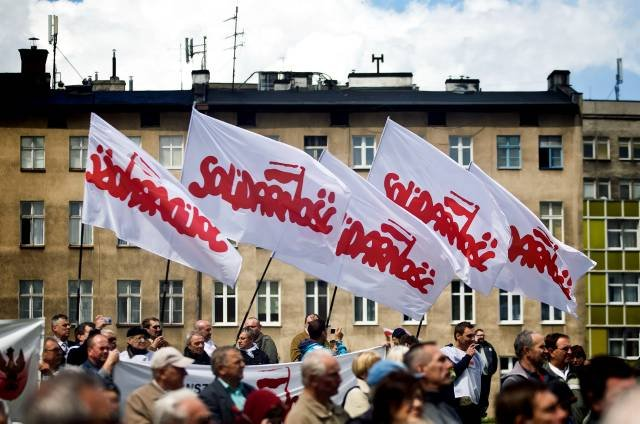 Flags for the Solidarity Party of Poland flying in the breeze against an urban backdrop during a rally